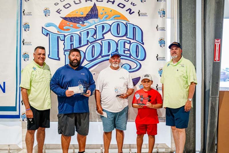 A group of men are standing in front of a tarpon rodeo sign.