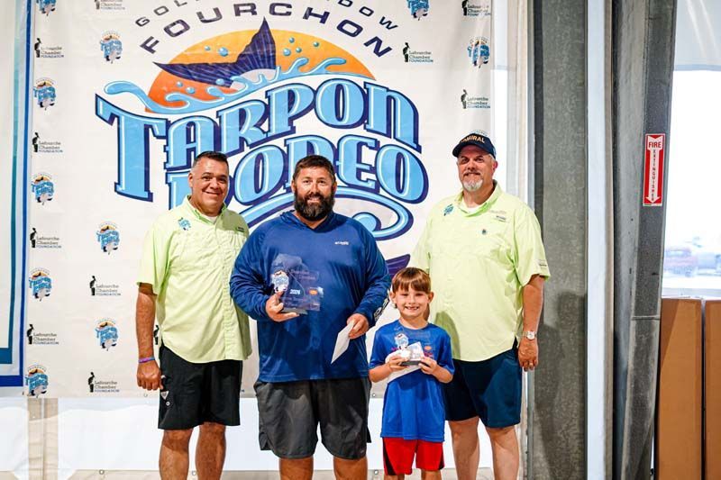 A group of men standing next to each other in front of a tarpon rodeo banner.