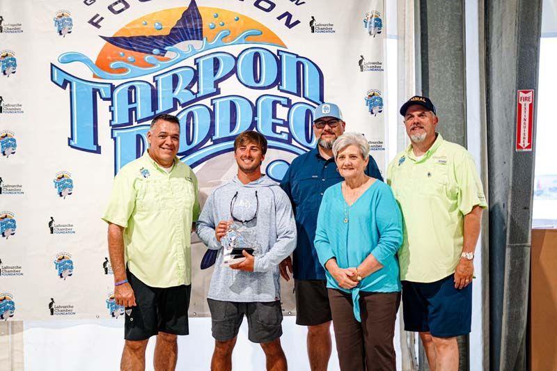 A group of people are posing for a picture in front of a tarpon rodeo banner.