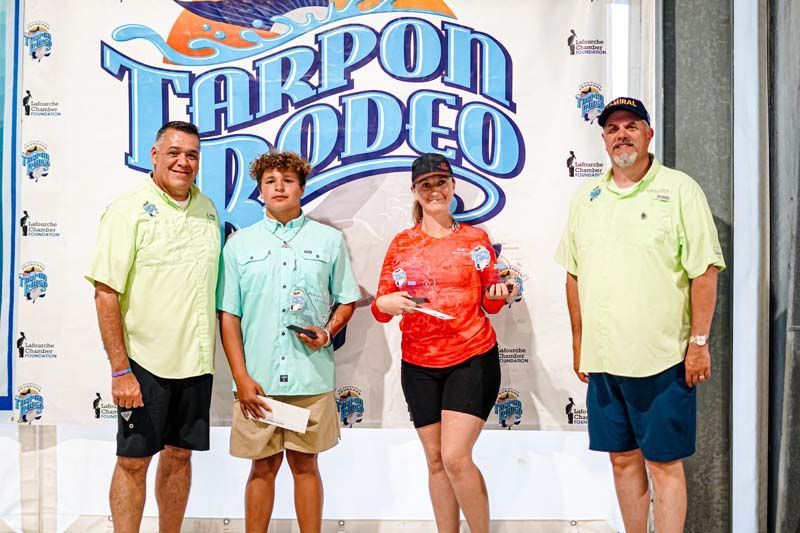 A group of people standing in front of a tarpon rodeo sign.