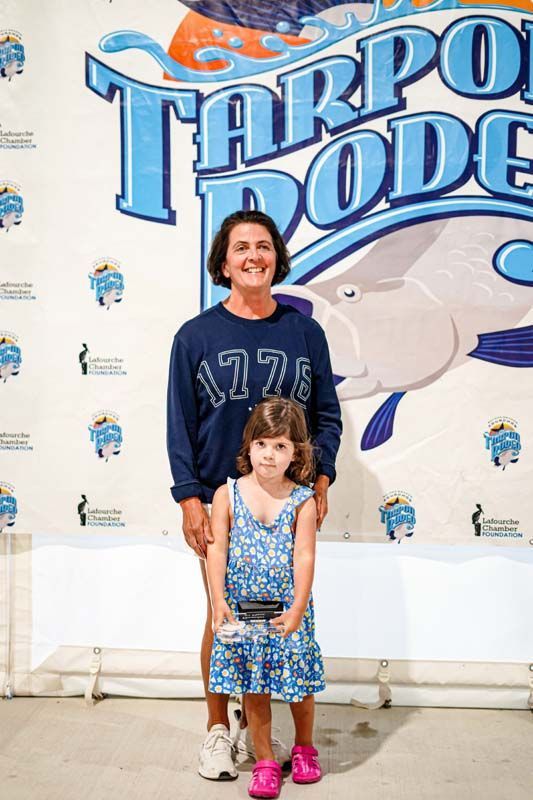 A woman and a little girl are standing in front of a tarpon pool sign.