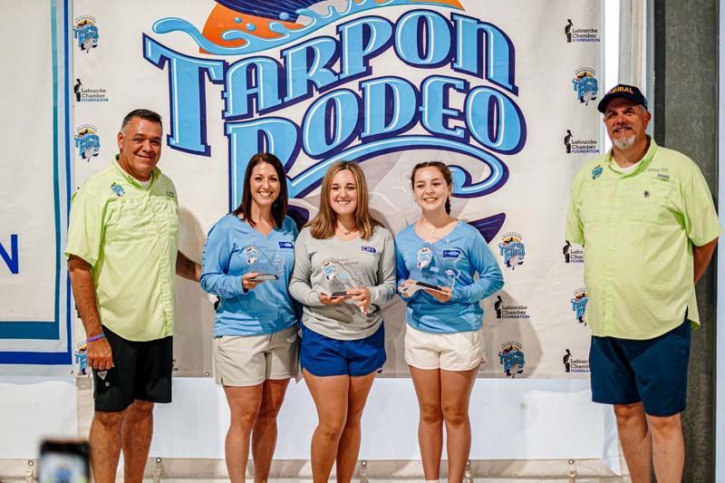 A group of people standing in front of a tarpon rodeo sign.