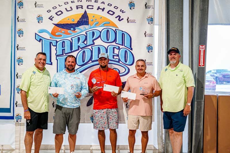 A group of men are posing for a picture in front of a tarpon rodeo banner.