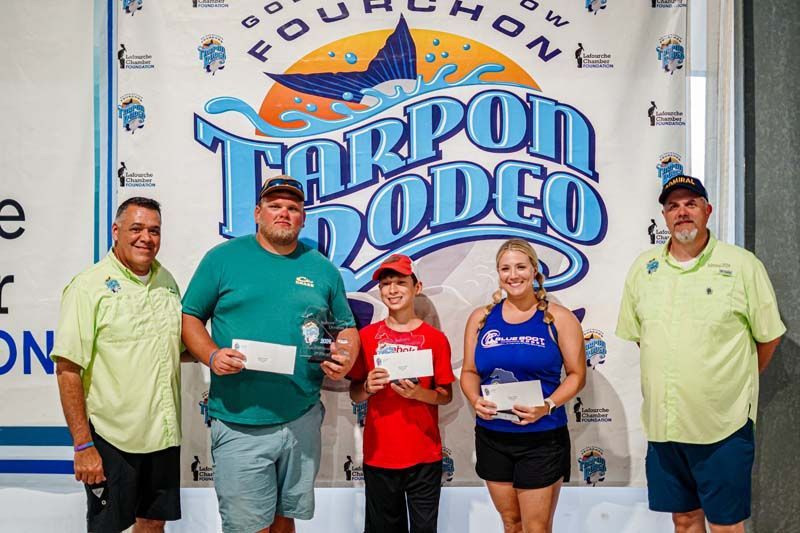 A group of people standing in front of a tarpon rodeo banner