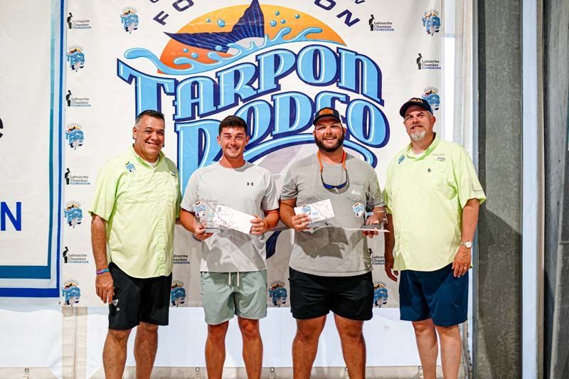 A group of men are standing in front of a tarpon rodeo sign.