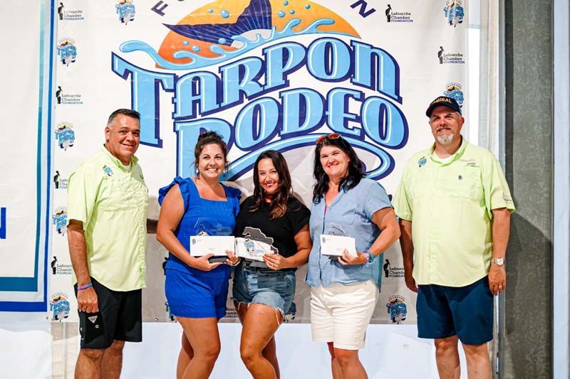 A group of people are posing for a picture in front of a tarpon rodeo sign.