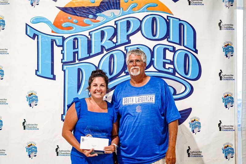 A man and a woman are posing for a picture in front of a tarpon rodeo sign.