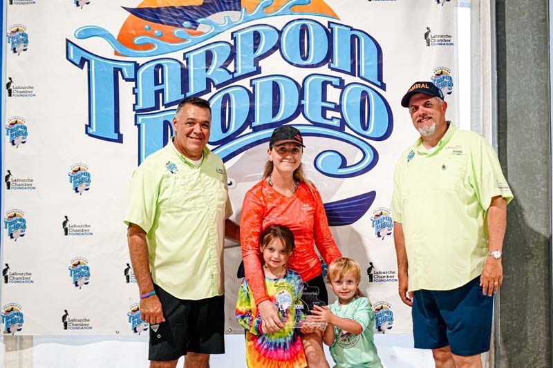 A group of people standing in front of a tarpon rodeo sign.