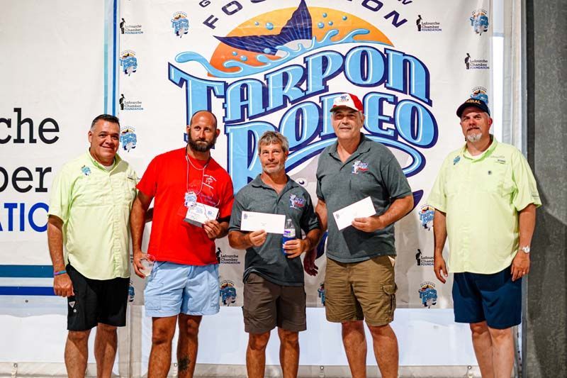 A group of men standing in front of a tarpon rodeo banner