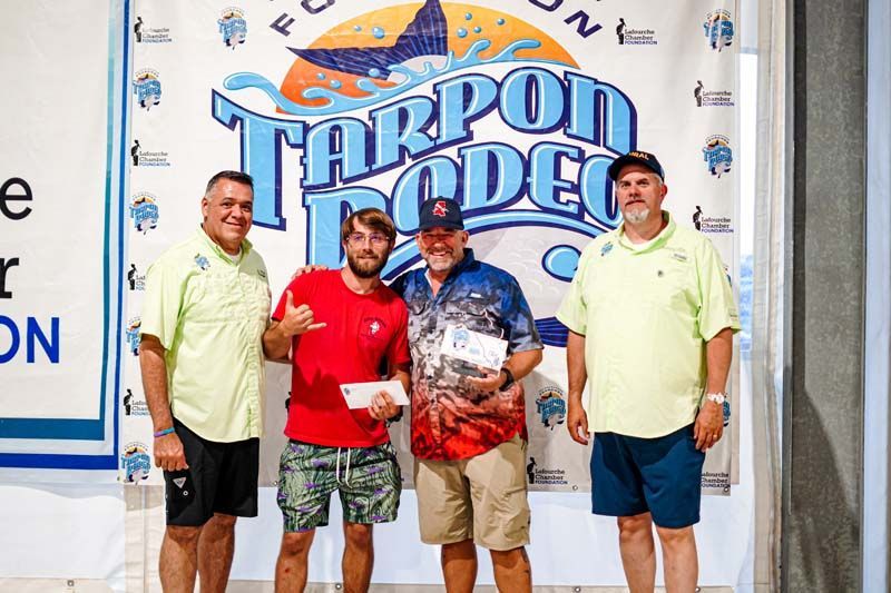 A group of men are standing in front of a tarpon rodeo sign.