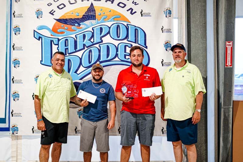 A group of men are posing for a picture in front of a tarpon dodge sign.