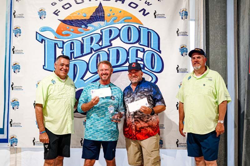 A group of men are standing in front of a tarpon rodeo banner.