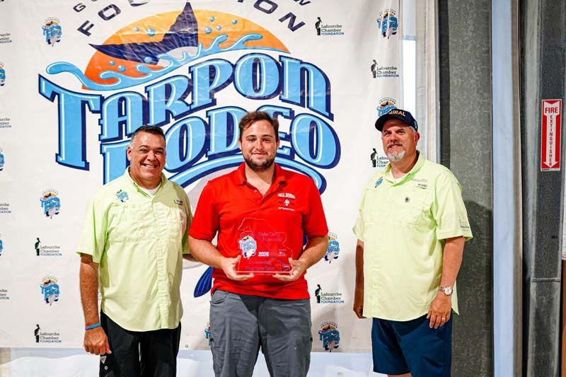 Three men are standing next to each other in front of a tarpon rodeo sign.