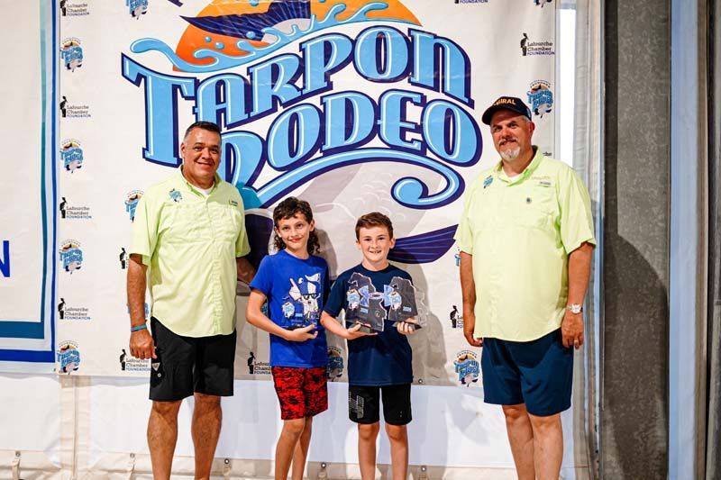 A group of men standing next to each other in front of a tarpon rodeo sign.