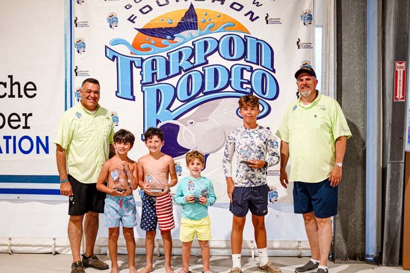 A group of young boys are standing in front of a tarpon rodeo banner.