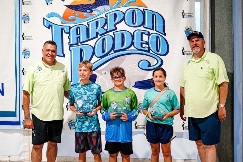 A group of people standing in front of a tarpon rodeo sign.
