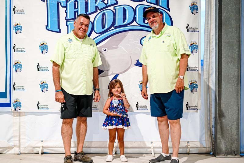 Two men and a little girl are standing in front of a sign.