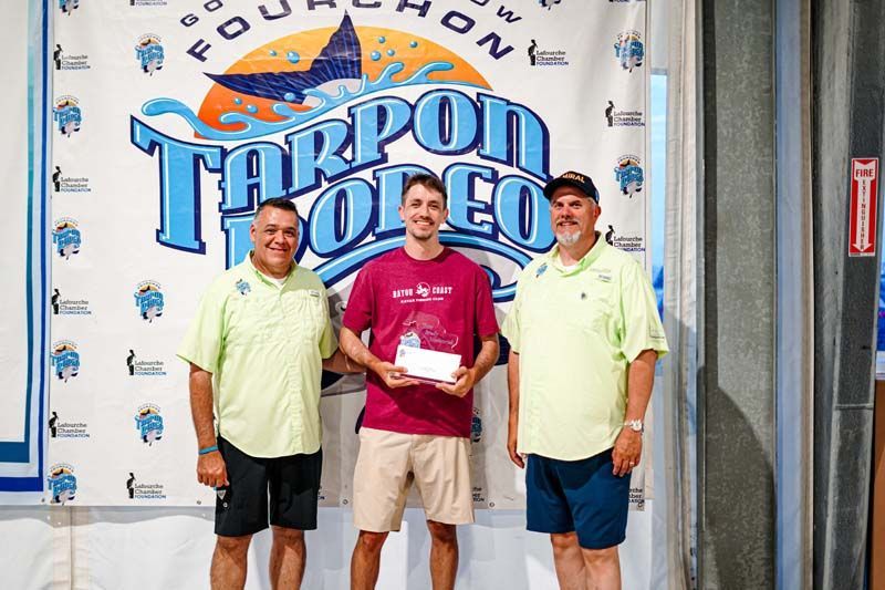 Three men are standing in front of a tarpon toleo banner.