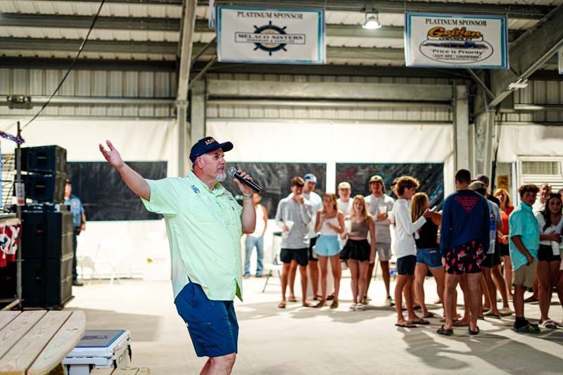 A man is standing in front of a group of people holding a microphone.