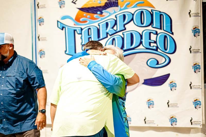 Two men hugging in front of a tarpon rodeo sign