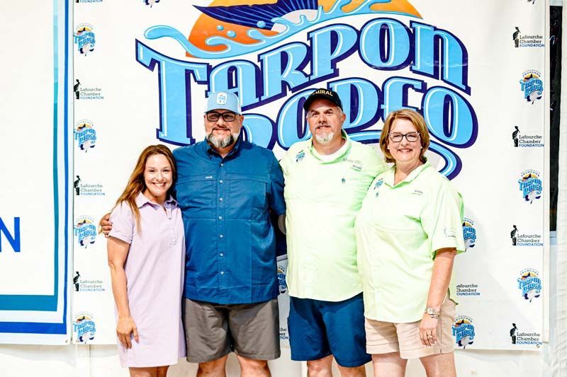 A group of people are posing for a picture in front of a tarpon dock sign.