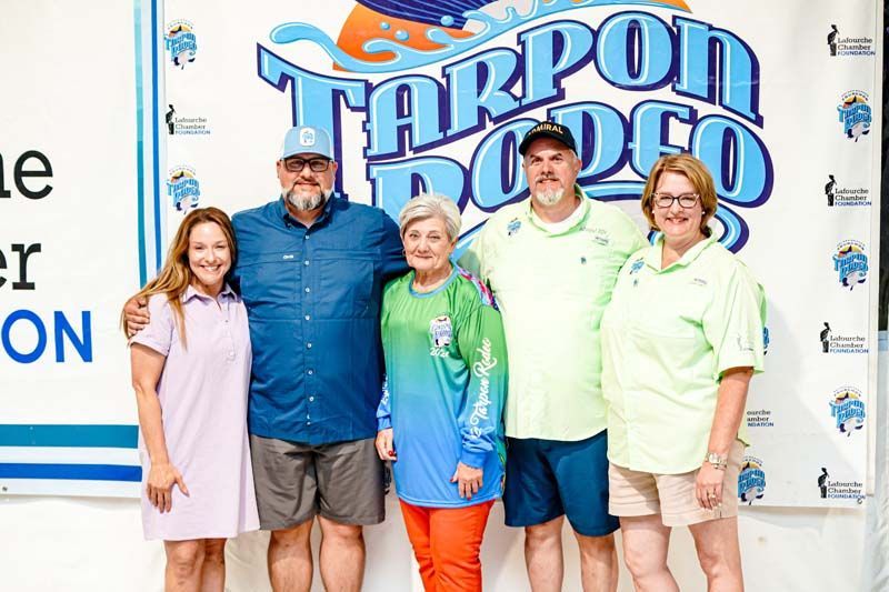 A group of people are posing for a picture in front of a tarpon rodeo sign.