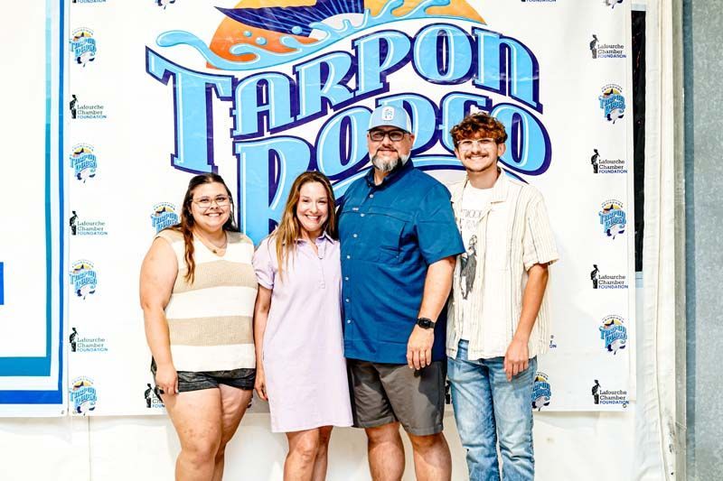 A group of people are posing for a picture in front of a tarpon rodeo sign.