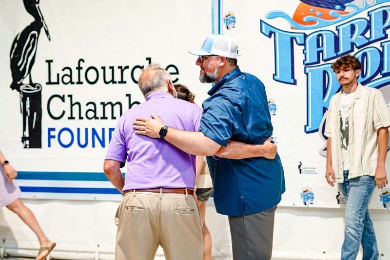 Two men hugging in front of a sign that says lafourche cham found