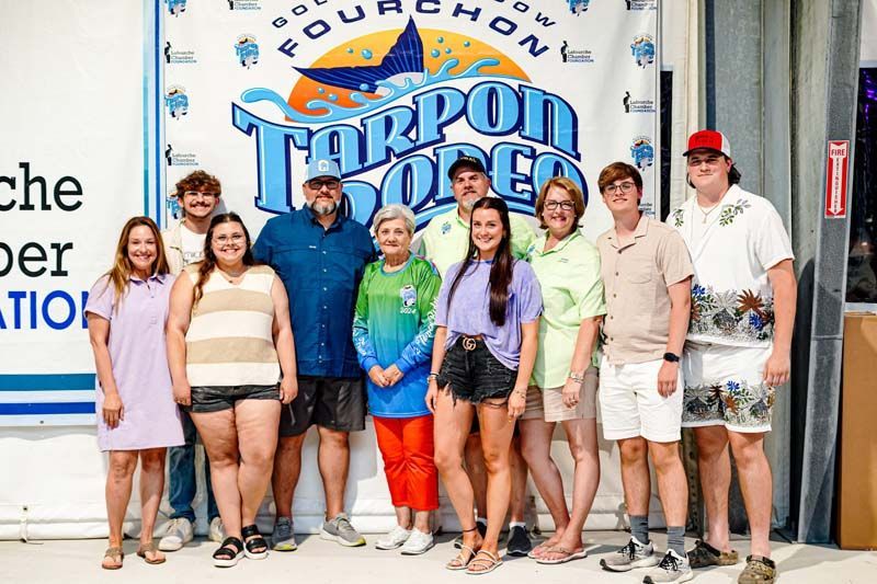 A group of people are posing for a picture in front of a tarpon open sign.