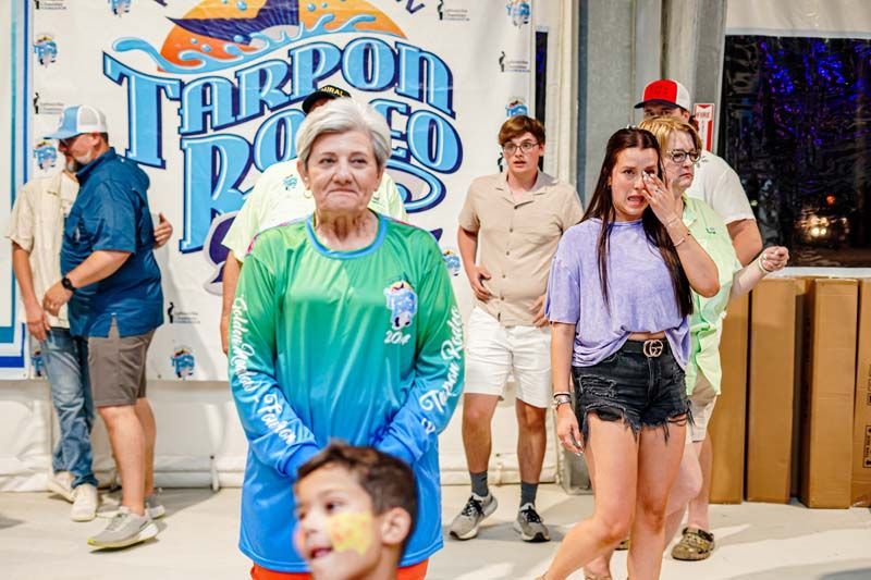 A group of people are standing in front of a sign that says tarpon rodeo.