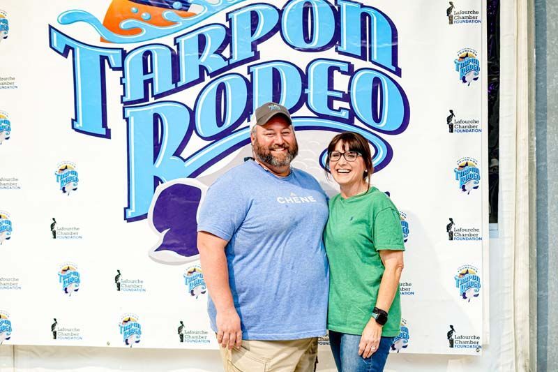 A man and a woman are posing for a picture in front of a tarpon rodeo sign.