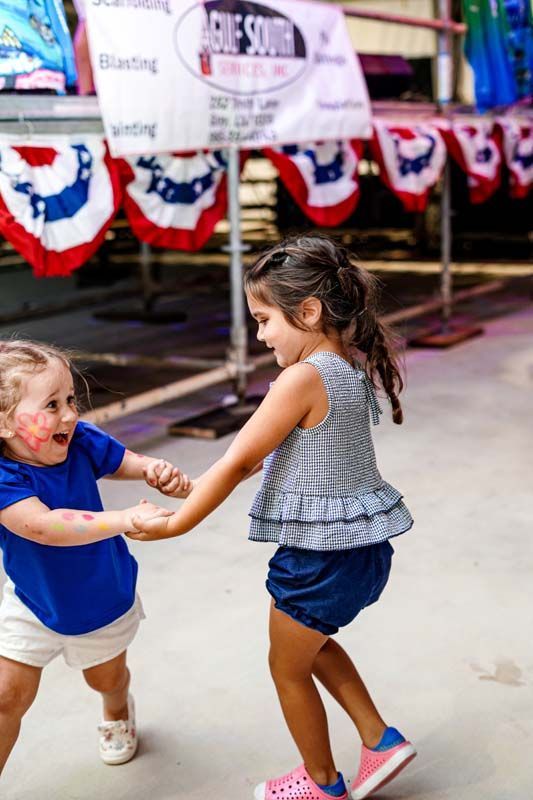 Two little girls are holding hands and dancing at a carnival.