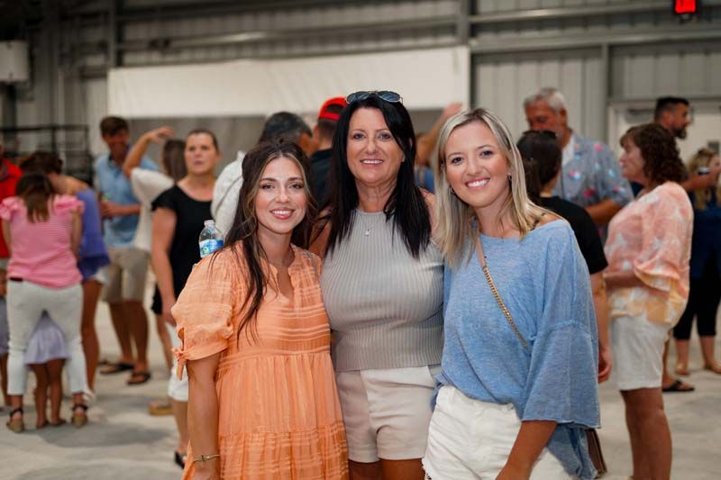 Three women are posing for a picture in front of a crowd of people.