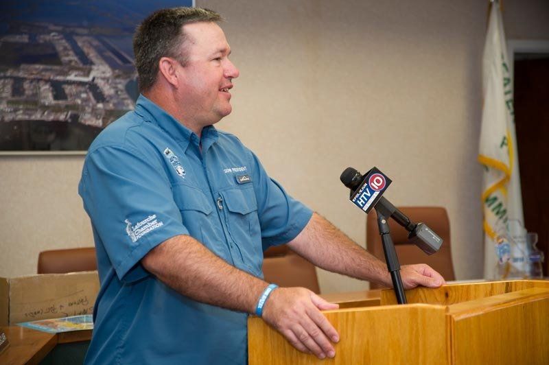 A man in a blue shirt is standing at a podium speaking into a microphone.