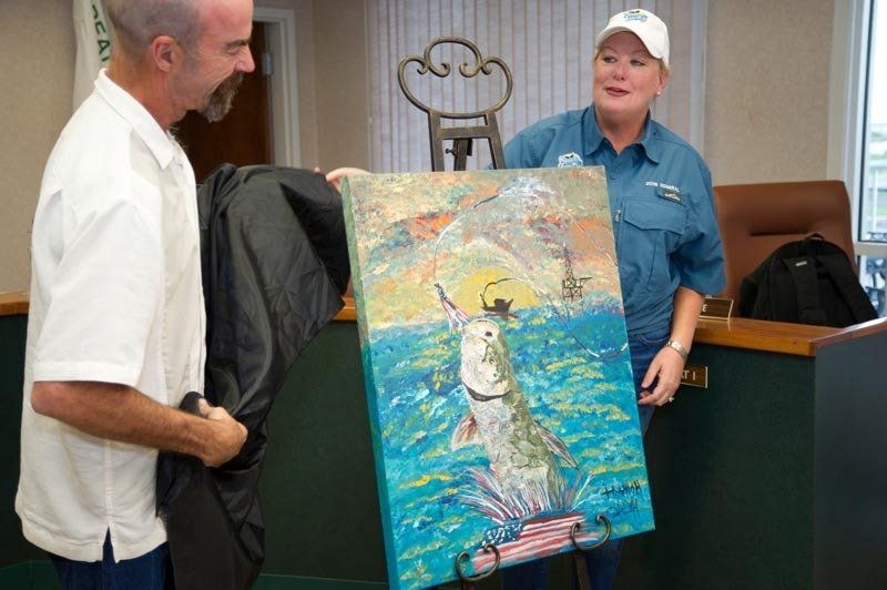 A man and a woman are holding a painting of a fish in the ocean.