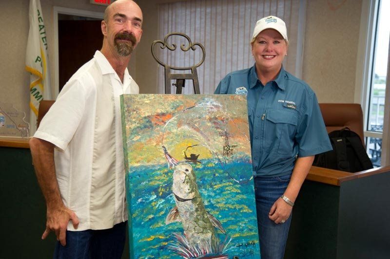 A man and a woman are holding a painting of a fish in the ocean.
