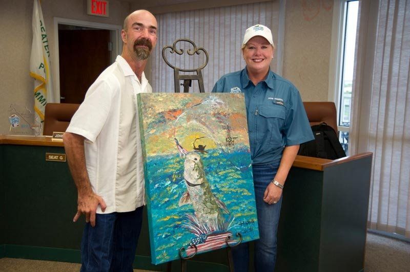 A man and a woman are holding a painting of a fish in the ocean.
