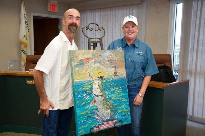 A man and a woman are holding a painting of a fish in the ocean.