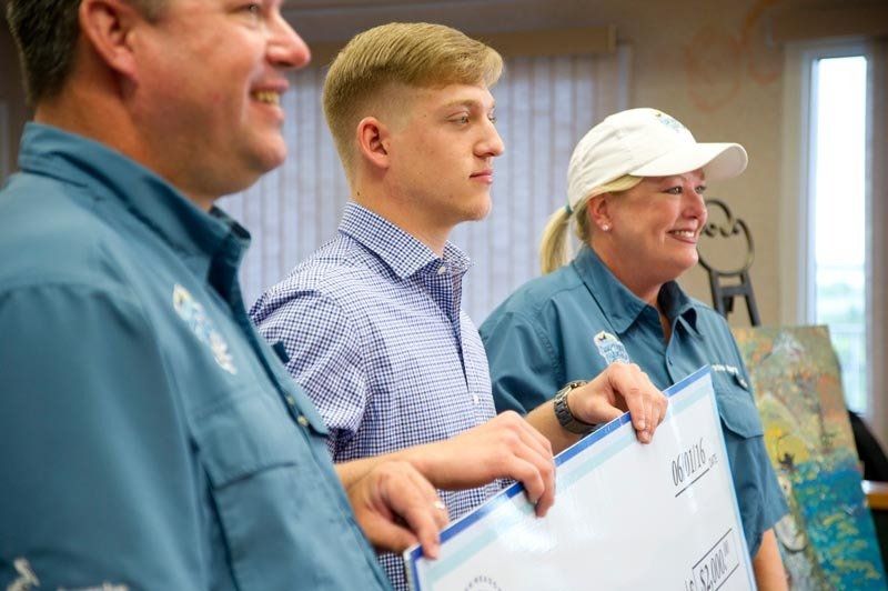 A man and two women are standing next to each other holding a check.