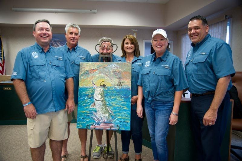 A group of people are standing around a painting on a stand.