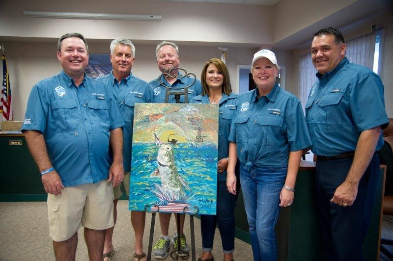 A group of people standing next to each other holding a painting.