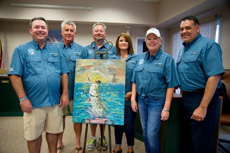A group of people standing around a painting of a fish in the ocean.