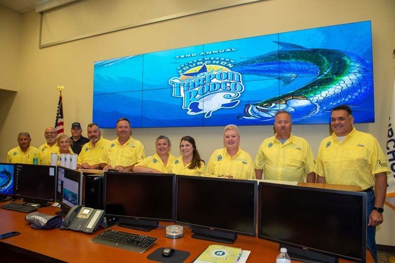 A group of people in yellow shirts are standing in front of computer monitors.