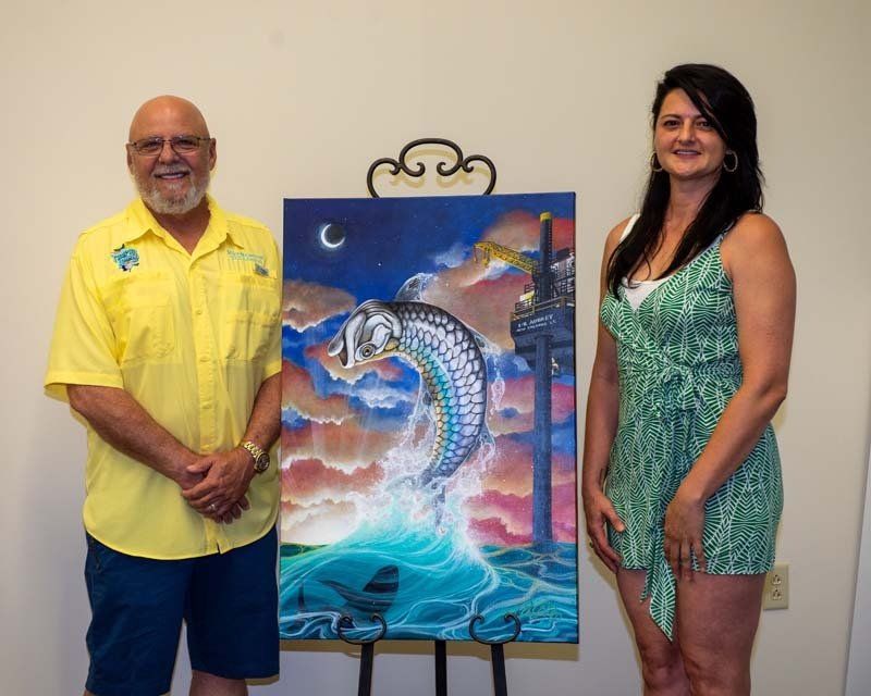 A man and a woman are standing next to a painting on an easel.