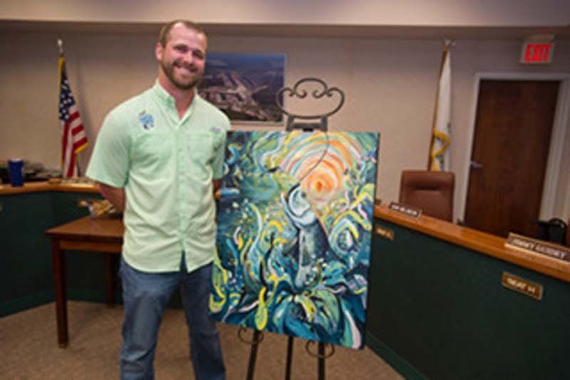 A man is standing in front of a painting on an easel.