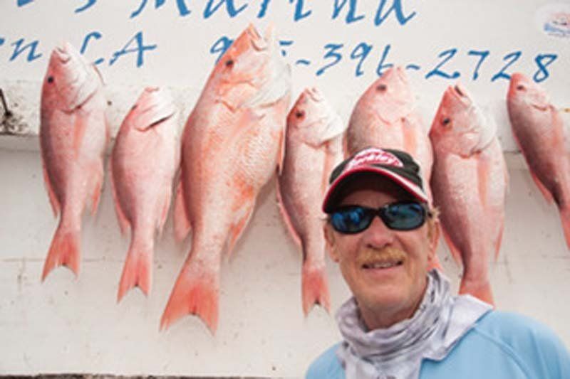 A man is standing in front of a wall of red fish.