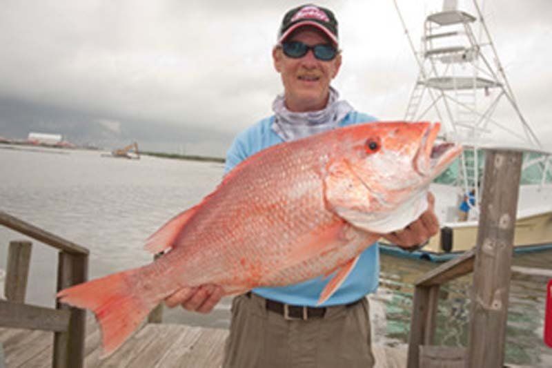 A man is holding a large red fish on a dock.