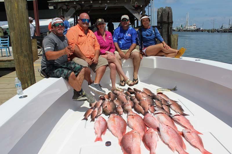 A group of people are sitting on a boat with a bunch of fish on the deck.