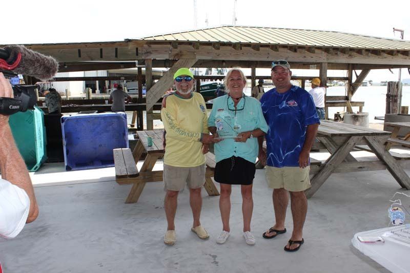 A man is taking a picture of three people standing in front of a picnic table