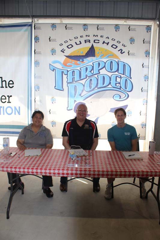 Three people sitting at a table in front of a tarpon rodeo sign